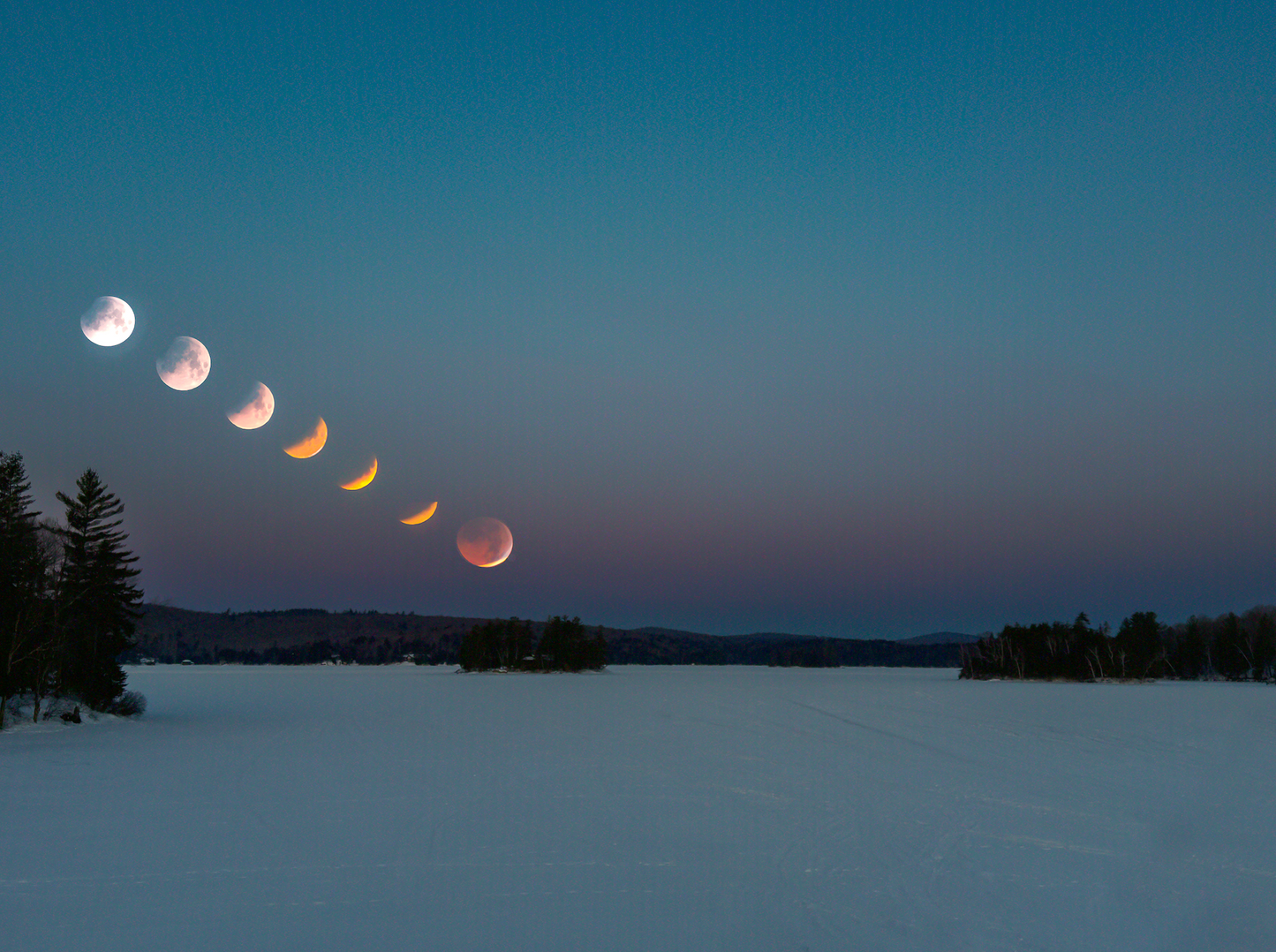 Phases of a lunar eclipse over a snowy landscape with trees.