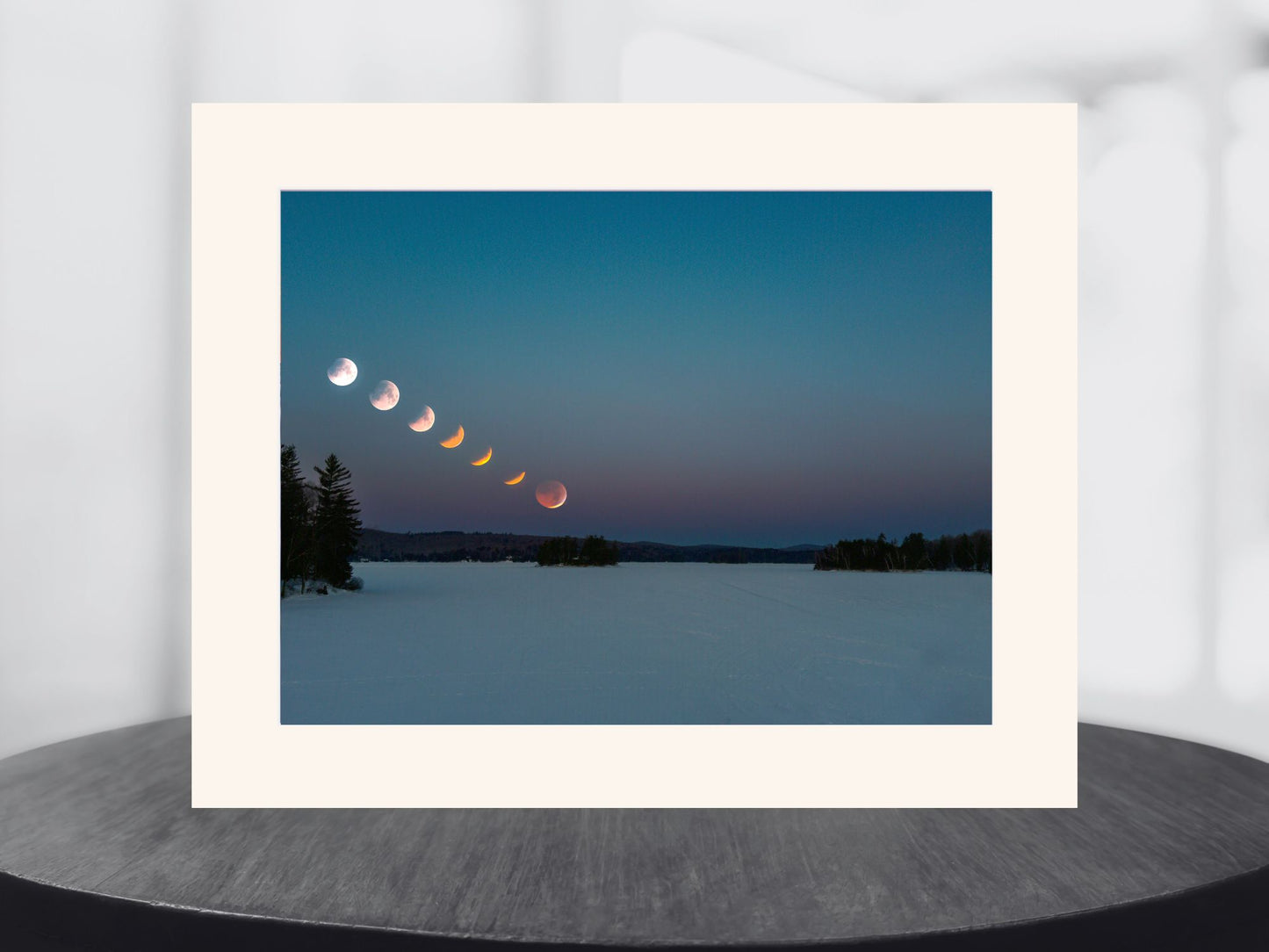 Framed photograph of a lunar eclipse sequence over a snowy landscape.