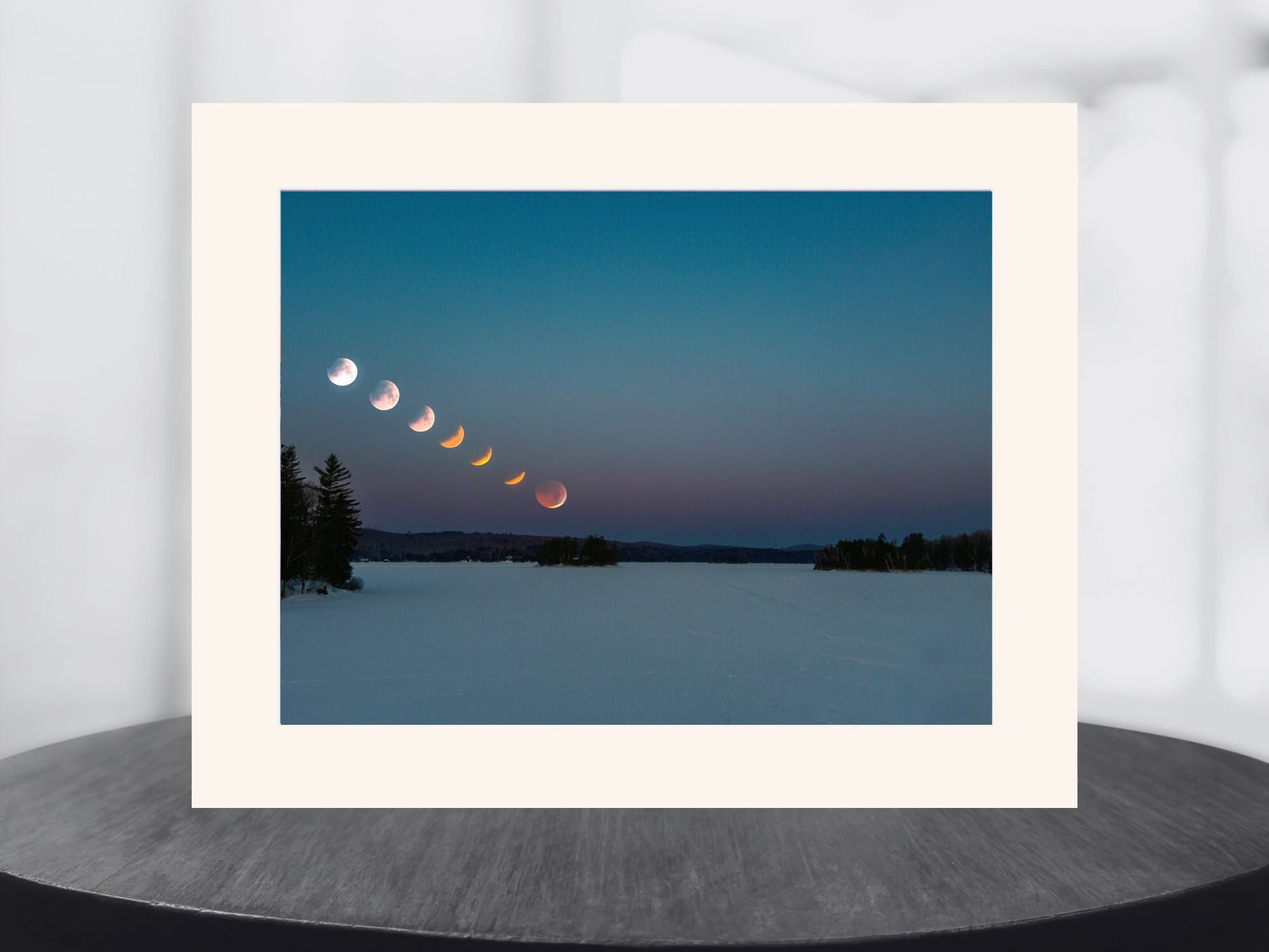 Framed photograph of a lunar eclipse sequence over a snowy landscape.