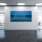 A framed or frameless landscape wall art print showing a calm lake at dusk with blue sky, dark tree silhouettes, and a moon near the horizon, displayed on a white wall in a modern office interior with glass walls and ceiling lights.