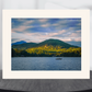 landscape art print depicting a lake with green mountains and a small boat under a cloudy sky, displayed in a white matte border.