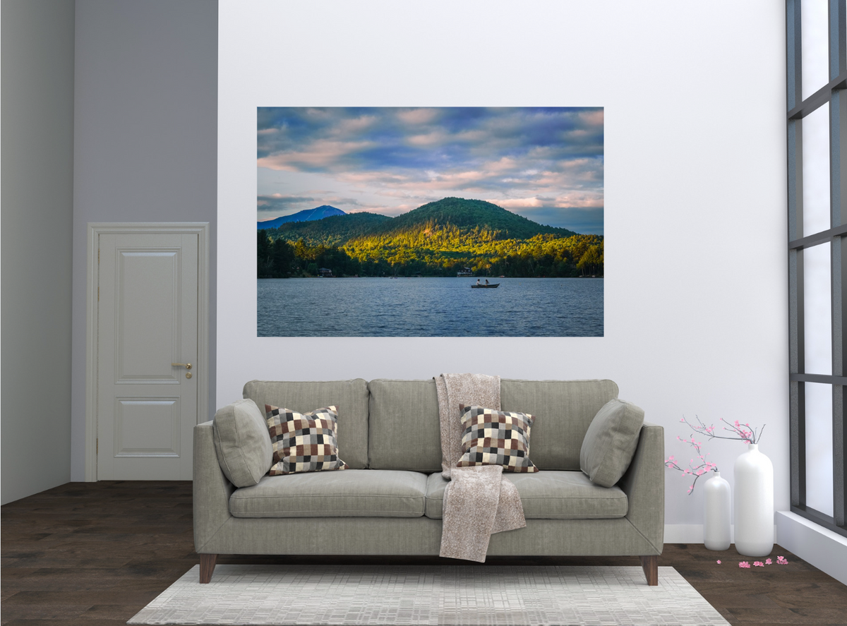 A framed landscape wall art print showing a mountain range over a lake with a small boat, displayed above a light gray sofa in a modern living room setting.