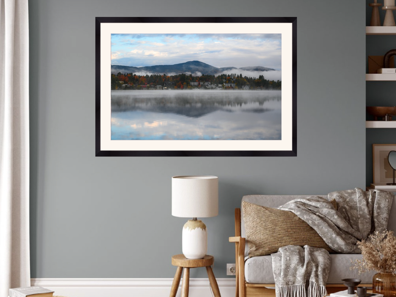 A framed landscape art print of a misty mountain lake scene, displayed on a gray wall above a sofa in a modern living room setting.
