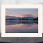 A matted landscape art print of a serene lake sunset with pink and purple clouds reflected in the water