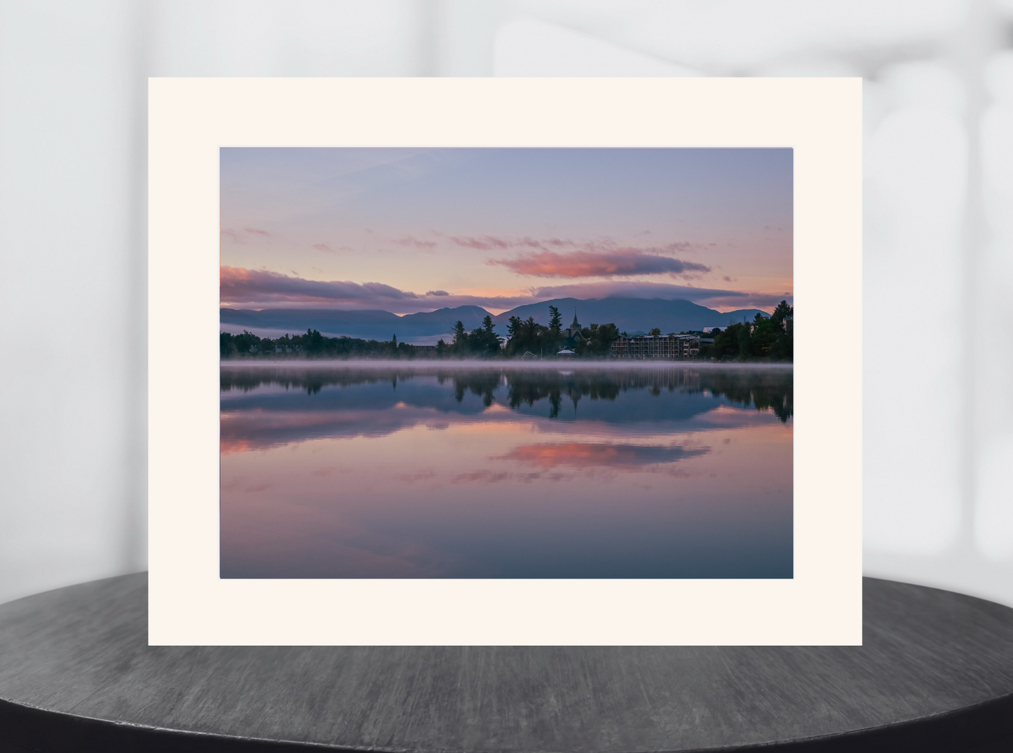 A matted landscape art print of a serene lake sunset with pink and purple clouds reflected in the water