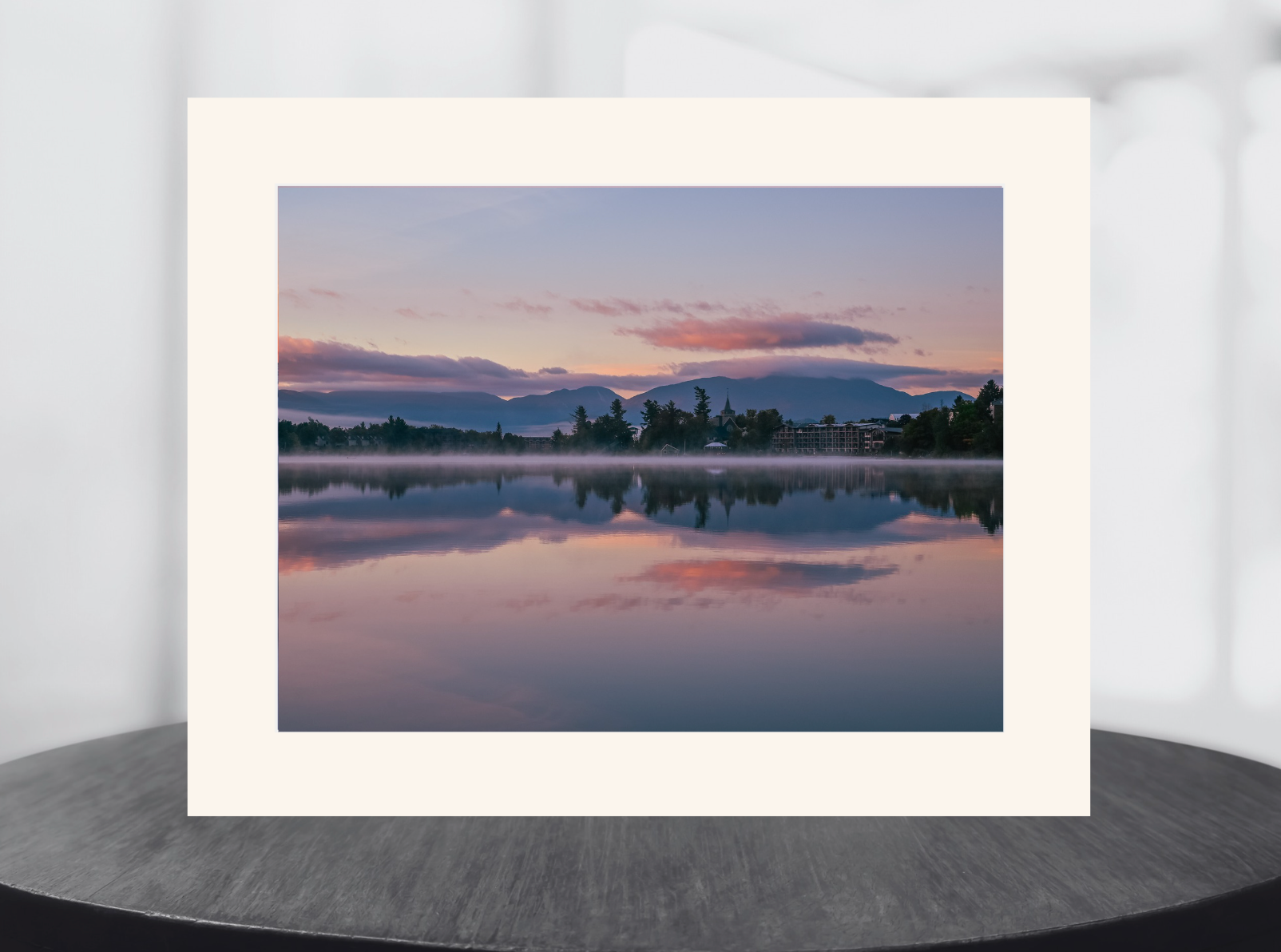 A matted landscape art print of a serene lake sunset with pink and purple clouds reflected in the water