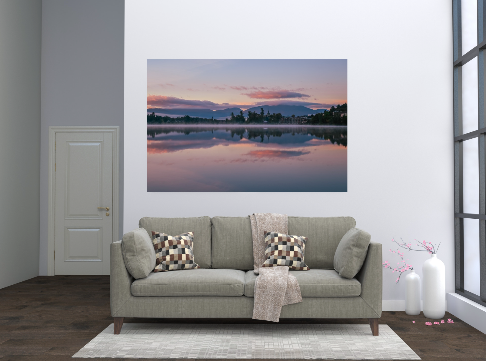 A large rectangular wall art print showing a calm lake reflection at sunset, displayed above a light gray sofa in a modern living room setting.